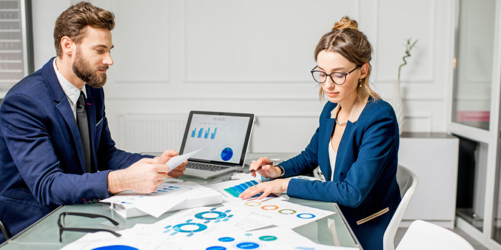 A man and a woman sit at a desk looking at charts and graphs